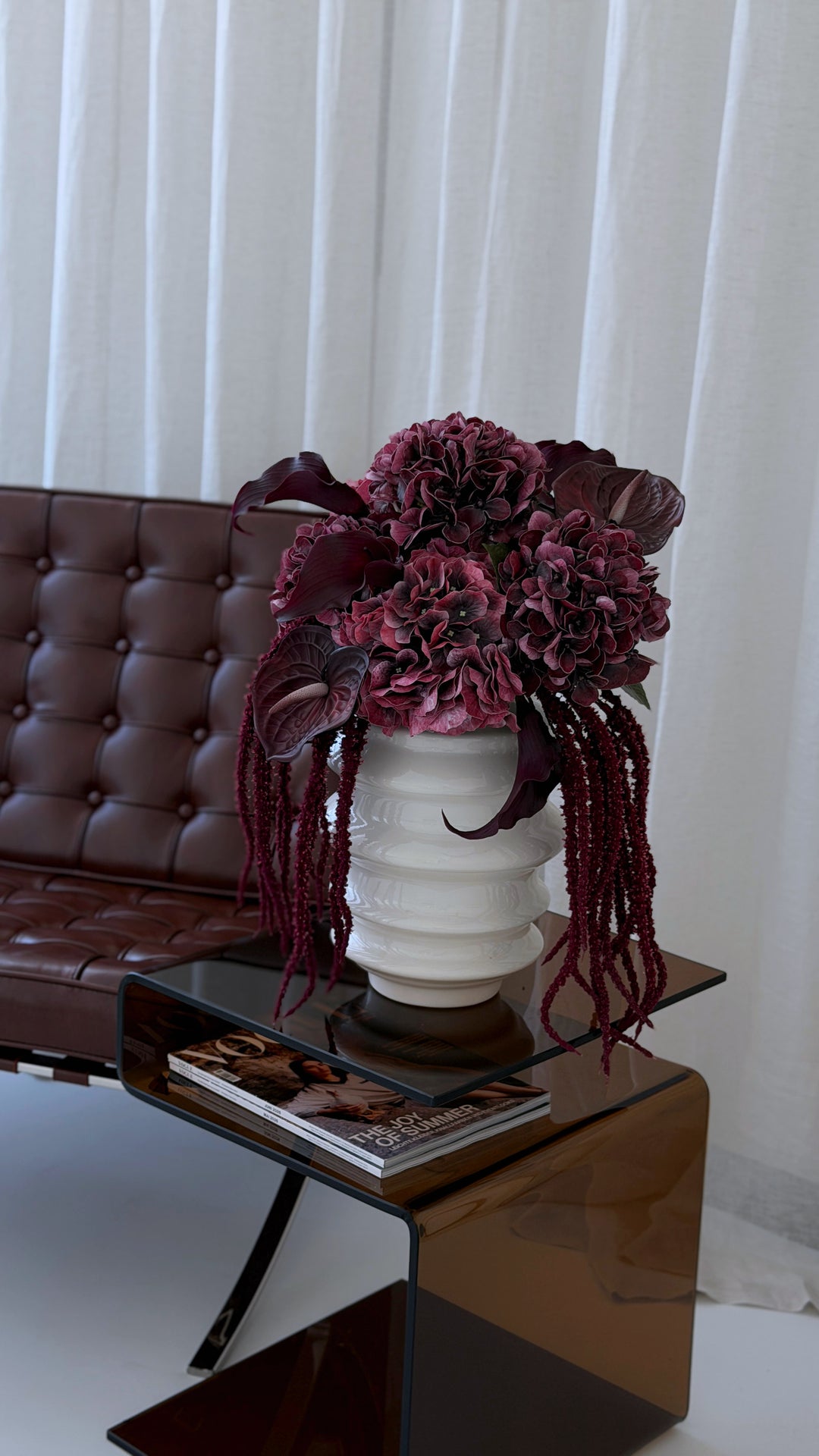 Burgundy- und Grün-Arrangements in Silber- und Keramikvase auf Travertin-Tisch vor cremefarbenem Sofa